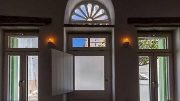 A door with a frosted glass panel, flanked by two windows with green shutters, and a decorative arch above.