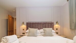 Cama bem arrumada com travesseiros, uma luminária de cabeceira e uma toalha dobrada no chão.