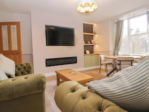 Ein Wohnzimmer mit einer Couch, einem Couchtisch, einem an der Wand montierten Fernseher, einem Kamin und einem Fenster mit Vorhängen.