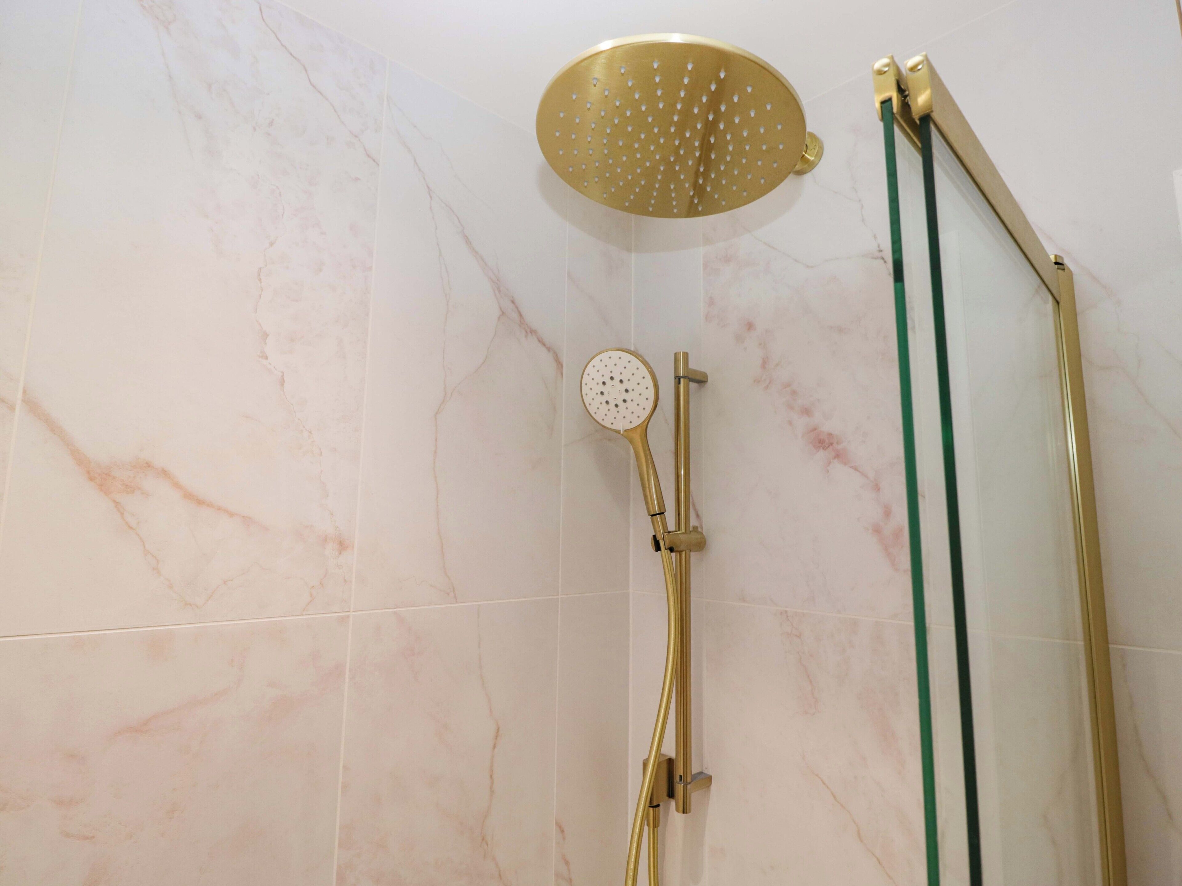 A bathroom with a gold showerhead, a handheld shower, and a glass-enclosed shower stall.