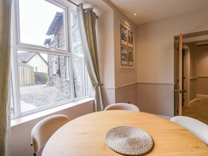 Ein Essbereich mit einem runden Tisch, Stühlen, einer gewebten Tischmatte, einem Fenster mit Vorhängen und gerahmten Bildern an der Wand.