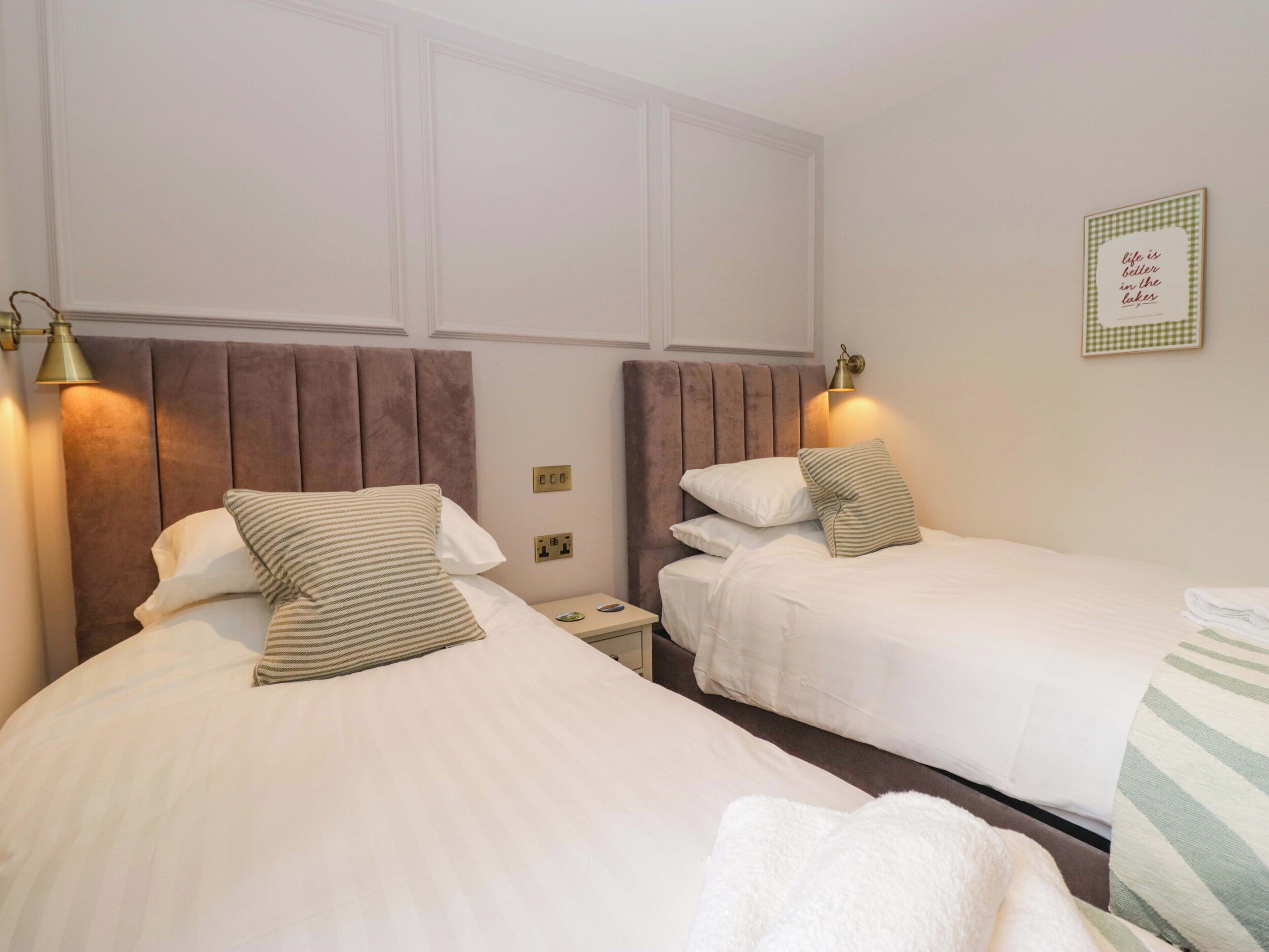 Une chambre d’hôtel avec deux lits, une table de chevet, une lampe et une citation encadrée au mur.