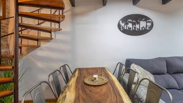 A dining area with a wooden table, metal chairs, a glass of water, a woven placemat, a gray sofa, and a wall-mounted artwork.