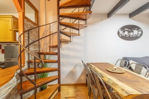 A spiral staircase with wooden steps and metal railings, a dining table with chairs, and a wall-mounted decorative plate. - Duplex in La Molina 5 Minutes from the Ski Slopes (Alp)
