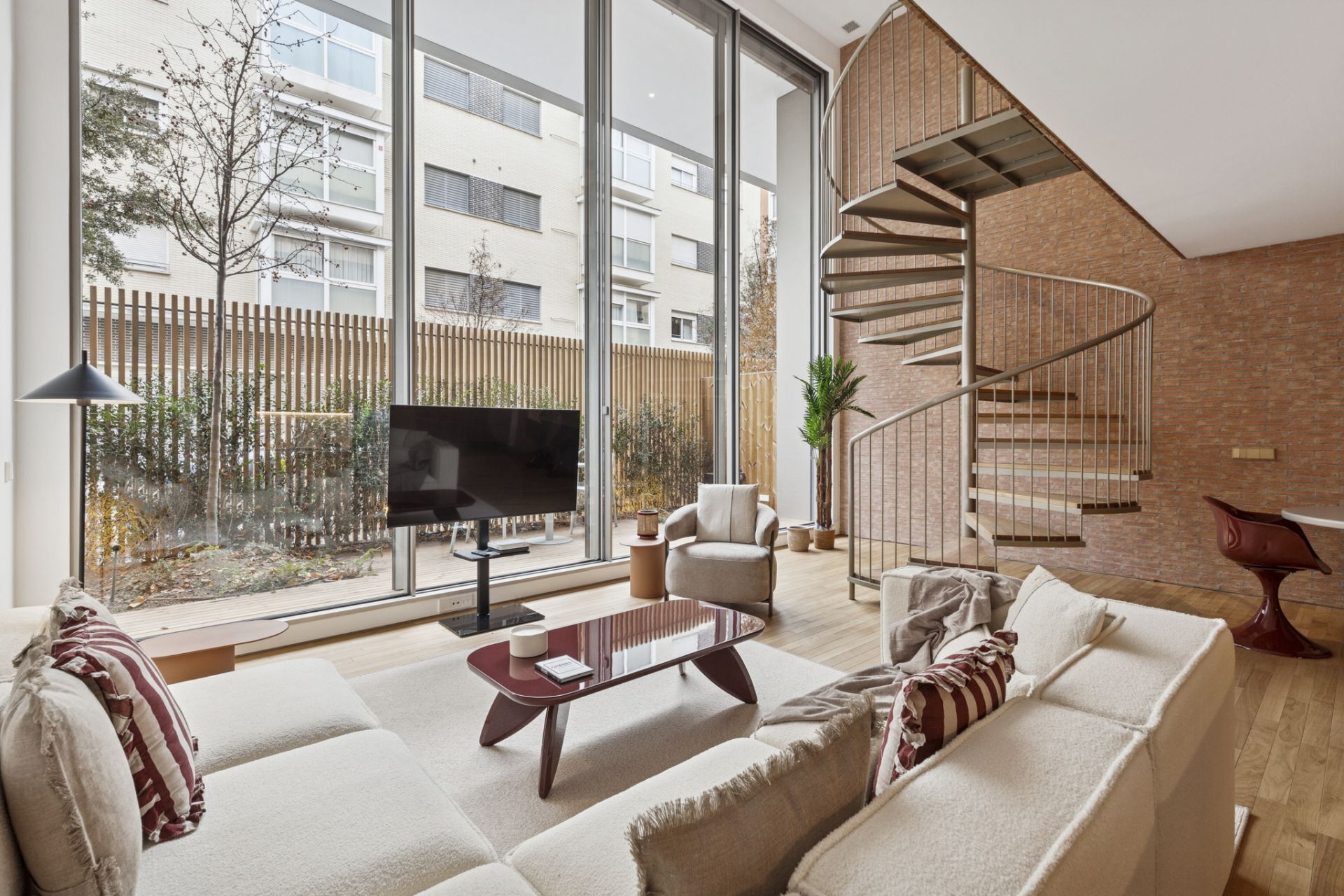 Ein modernes Wohnzimmer mit Sofa, Couchtisch, Fernseher und einer Wendeltreppe.