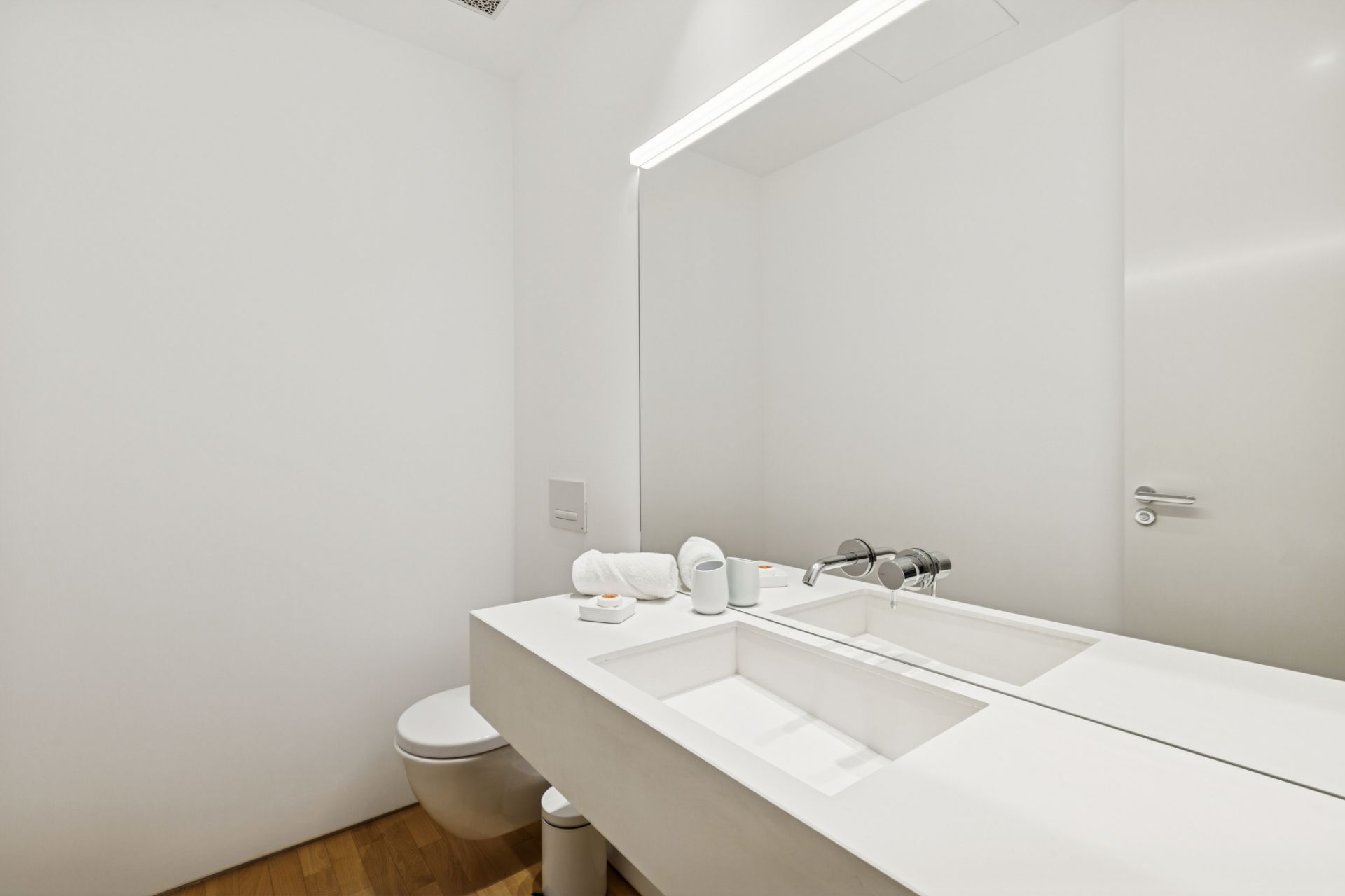 Une salle de bain moderne avec un grand miroir, deux lavabos, des toilettes et un luminaire.