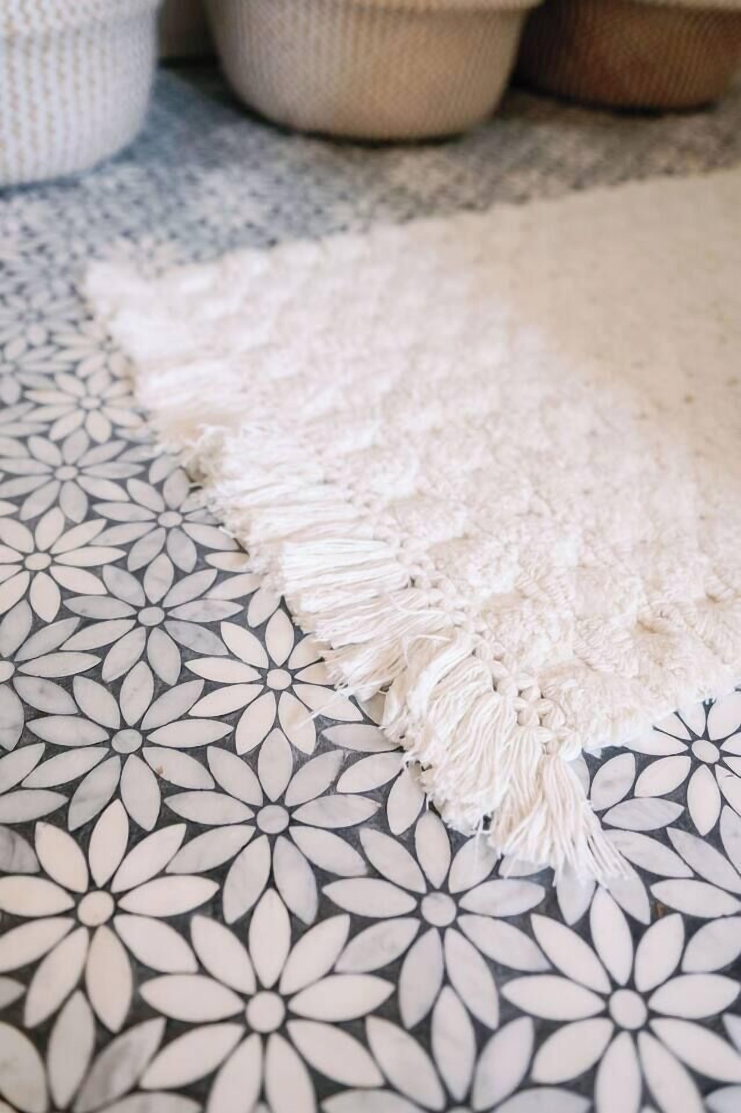 A patterned rug with a fringe edge on a floor.