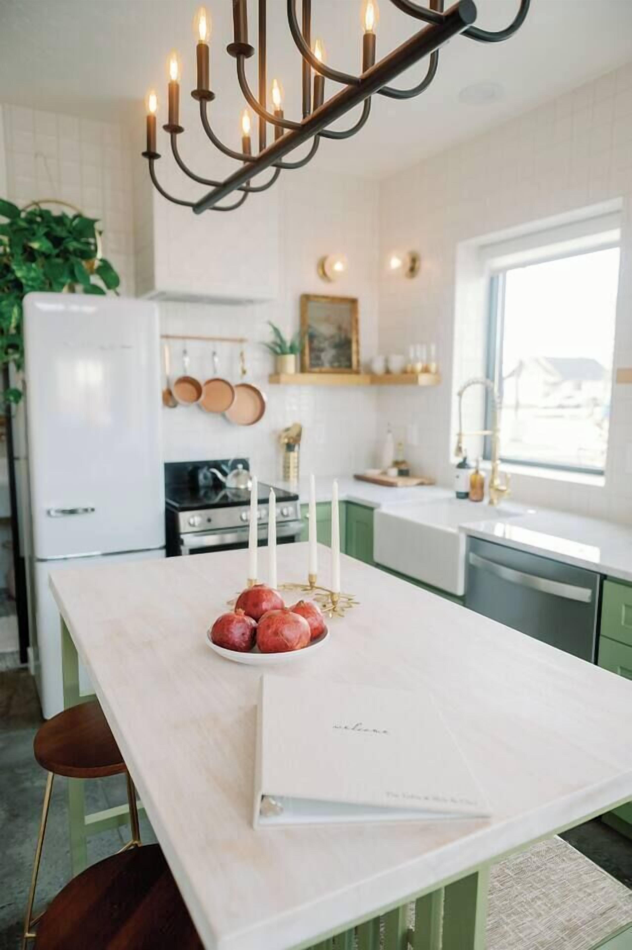 Une cuisine avec un îlot central, des meubles blancs, une cuisinière et une fenêtre.