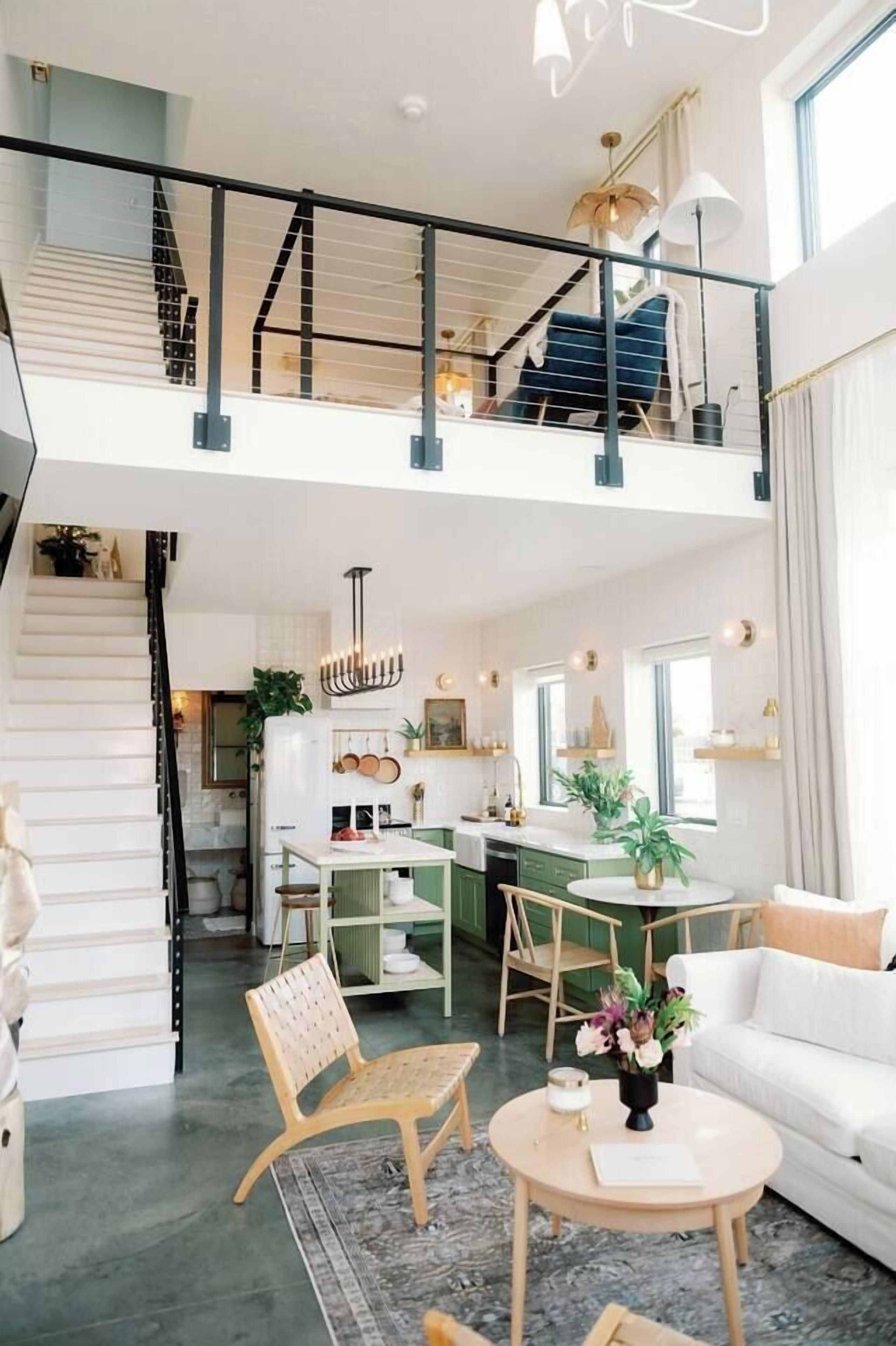 A spacious loft apartment with a high ceiling, a staircase leading to an upper level, a kitchen area, and a seating area with a round table.