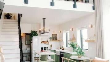 Um amplo apartamento duplex com teto alto, escada para um andar superior, cozinha e área de estar com mesa redonda.