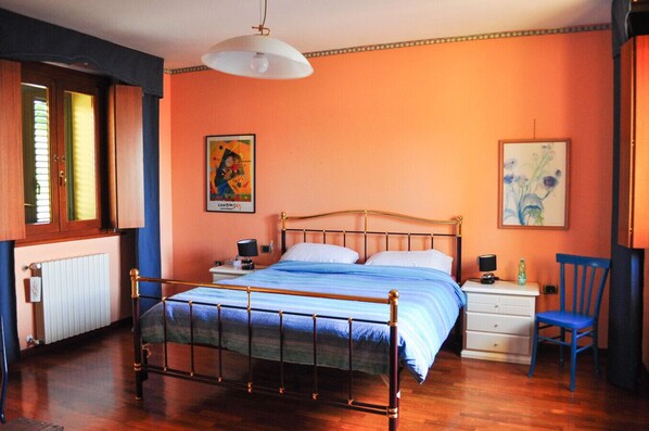 A bedroom with a bed, bedside tables, a chair, a radiator, and artwork on the walls.