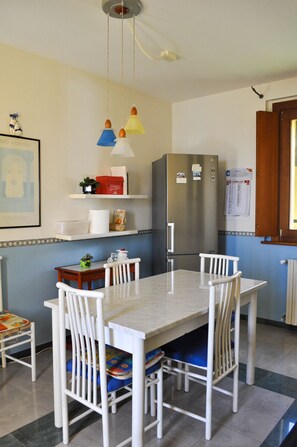 A dining area with a table, chairs, a refrigerator, and a wall-mounted calendar.