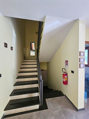 Un escalier avec des marches noires menant à un palier, un extincteur fixé au mur et une porte avec une signalétique indiquant une sortie de secours.