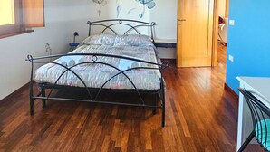 Ein Schlafzimmer mit Holzbalkendecke, einem Bett mit Metallgestell, einer Wandleuchte und einer Tür zu einem anderen Raum.