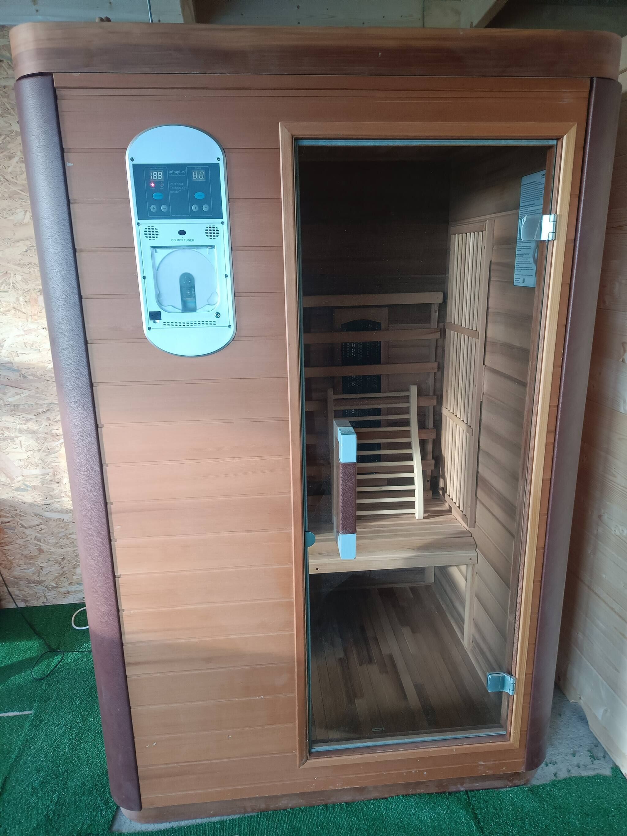 A sauna with a control panel, wooden benches, and a glass door.