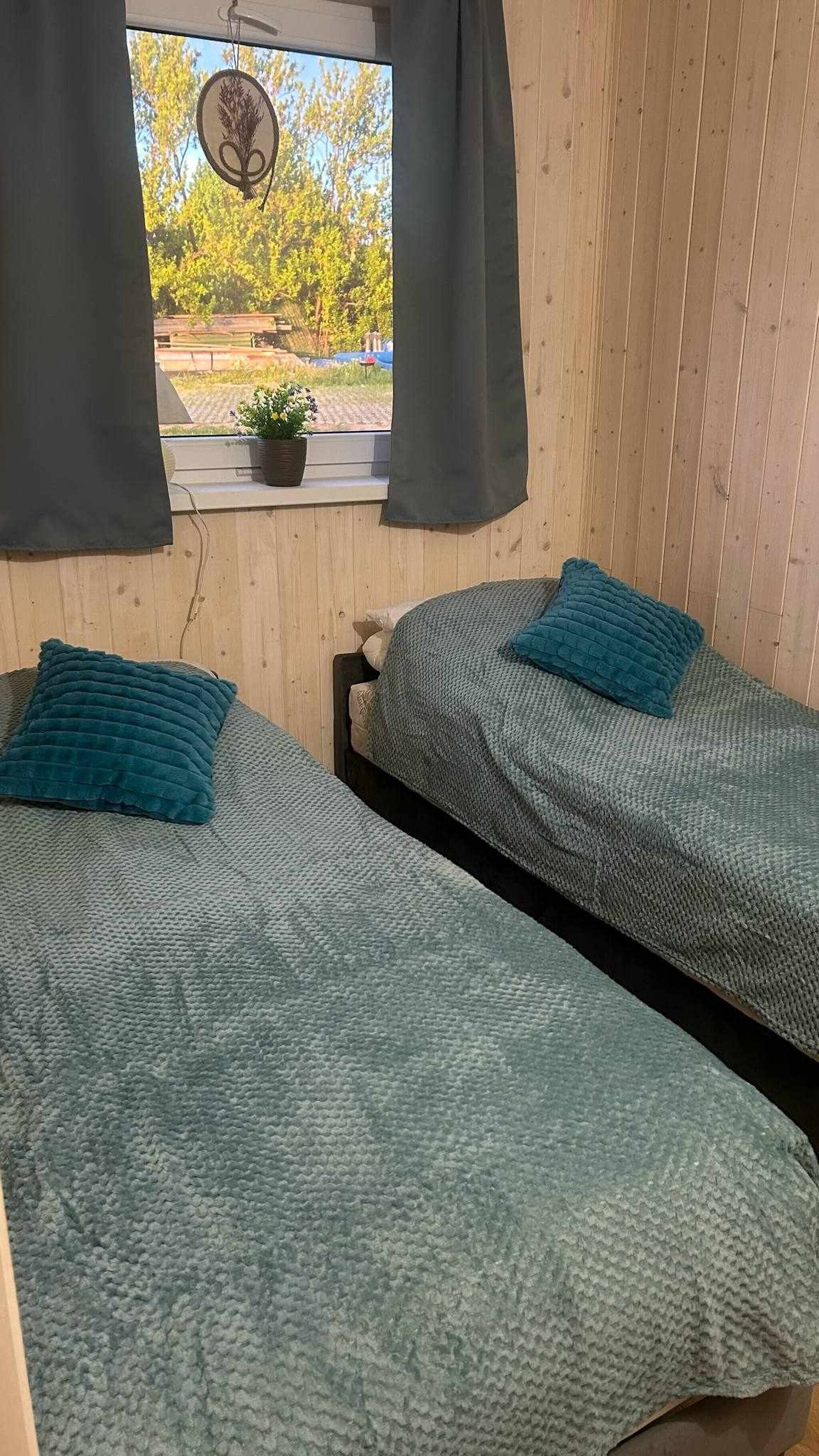 Une chambre avec deux lits, une fenêtre avec des rideaux, un objet décoratif suspendu et une plante en pot posée sur le rebord de la fenêtre.