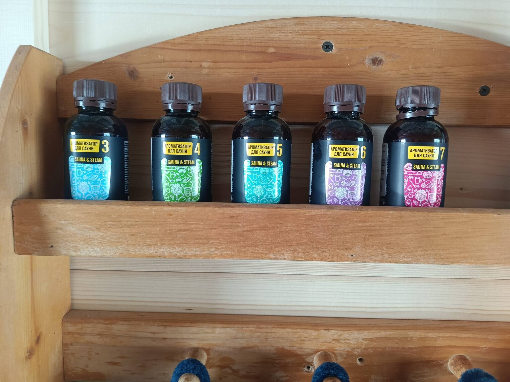 Een houten plank met vijf flessen, gelabeld van 3 tot 7, elk met een andere kleur en tekst die aangeeft dat het geurstoffen voor sauna’s en stoombaden zijn.