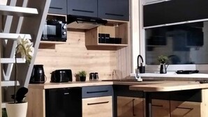 A modern kitchen with wooden cabinetry, a black stove, and a wooden dining table. - Domek nr 1 "błękitne Wzgórze" (gmina Brzuze)