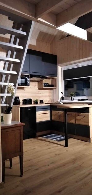 A modern kitchen with wooden cabinetry, a black stove, and a wooden dining table. - Domek nr 1 "błękitne Wzgórze" (gmina Brzuze)
