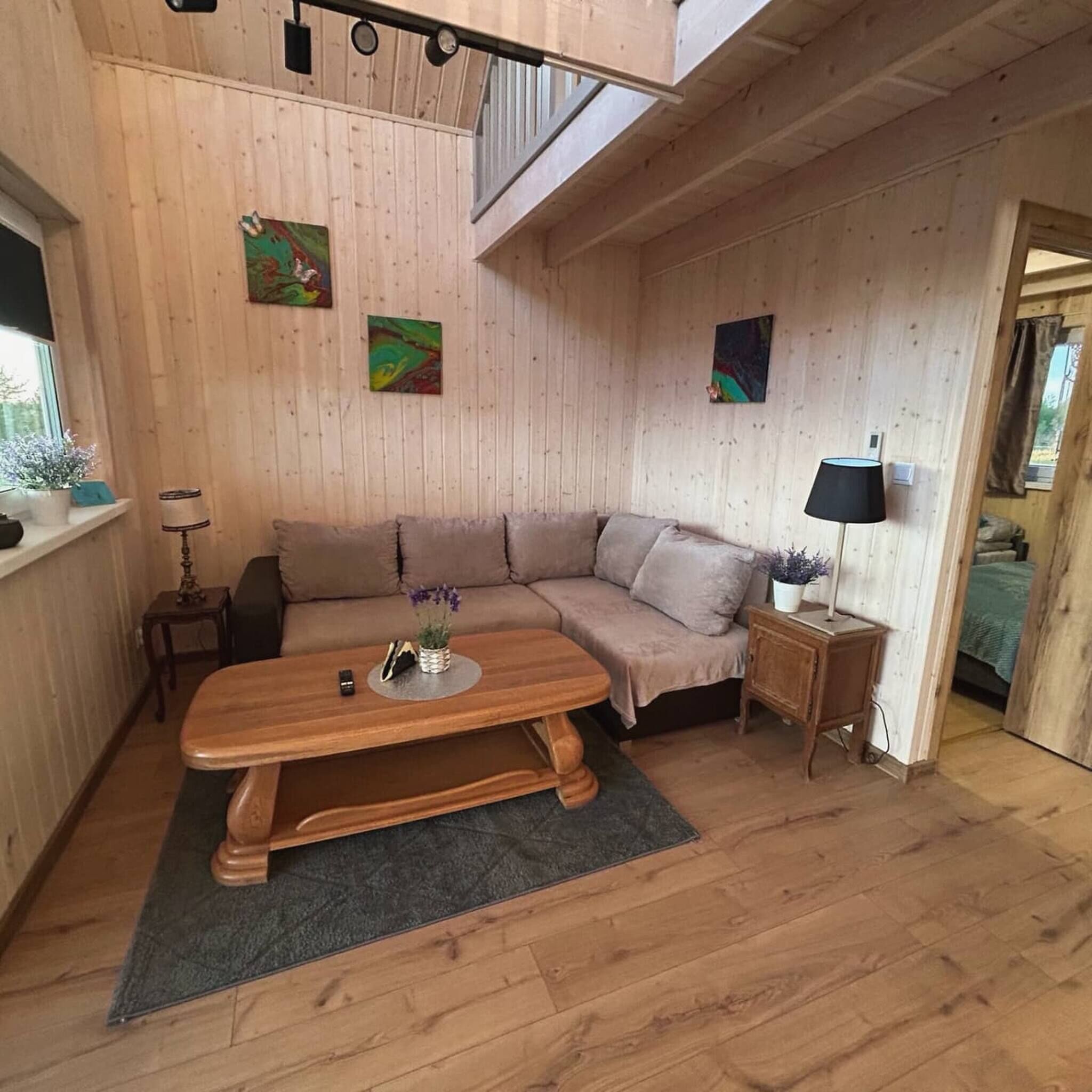 A cozy room with a wooden floor, a sofa, a small table with a vase, and a lamp.