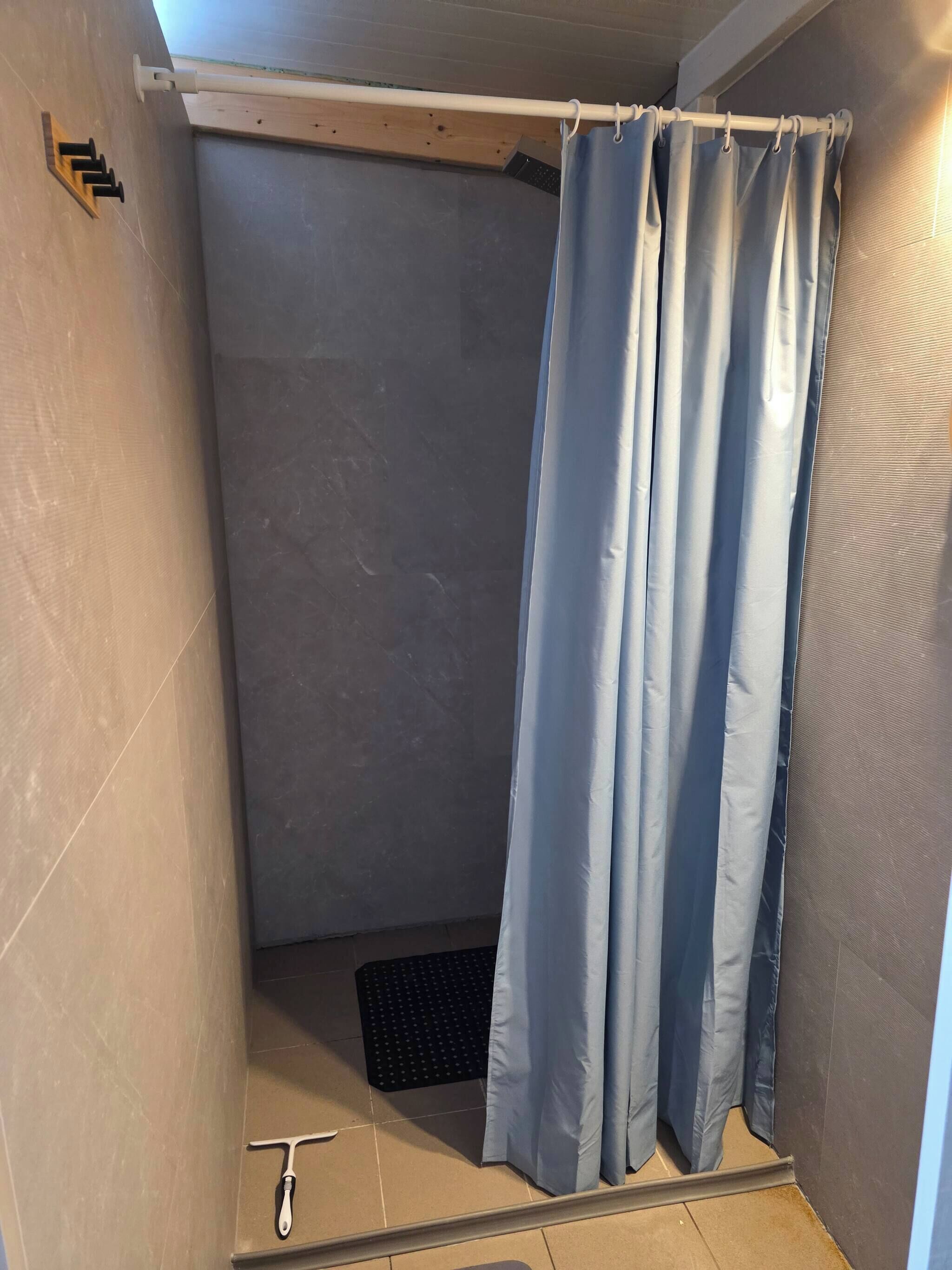 Ein kleiner, abgeschlossener Duschbereich mit blauer Duschvorhang, einer schwarzen Matte auf dem Boden und einem weißen Handtuchhalter an der Wand.