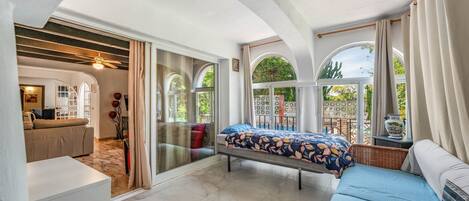 A bedroom with a bed, a sofa, a dining table, and a view of the outdoors.