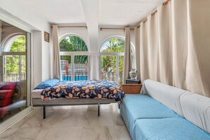 Una stanza con un letto, una poltrona, una finestra con tende e vista sul verde.