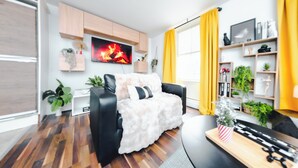 A modern living room with a fireplace, a black leather sofa, wooden flooring, and a yellow curtain. - Stylish 2BR Apartment on Brick Lane – Near Shoreditch (London)
