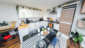 A compact kitchen with white cabinets, a dining table set with plates and cutlery, and a microwave. - Stylish 2BR Apartment on Brick Lane – Near Shoreditch (London)