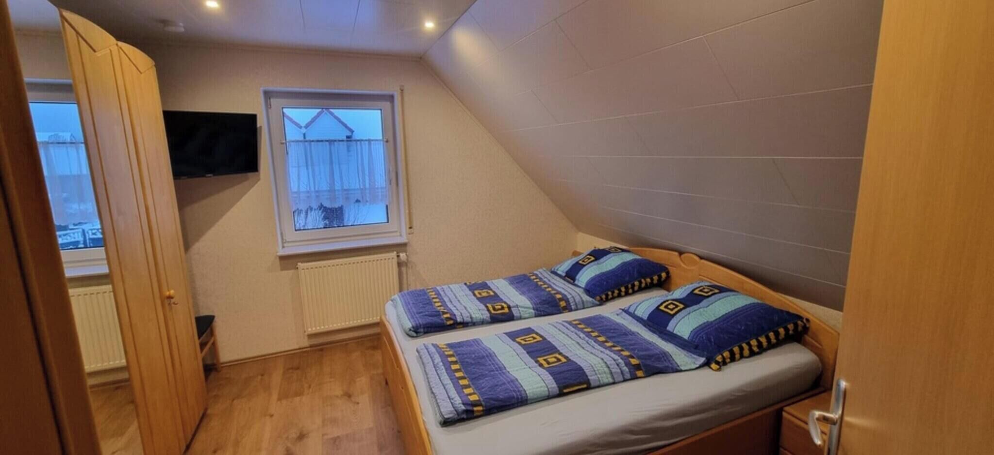 A small, single-bed room with a window, a radiator, and a wooden door.