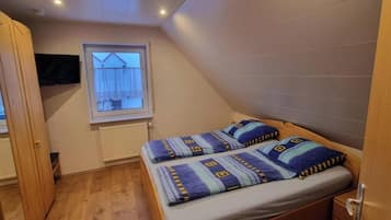 A small, single-bed room with a window, a radiator, and a wooden door.