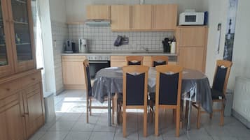 Een keuken met houten kastjes, een eettafel met stoelen, een magnetron en een waterkoker.