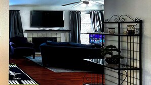 A living room with a sofa, armchair, TV, and a decorative plant. - A comfortable, restful stay designed for doctors and Medical Professionals (Houston)