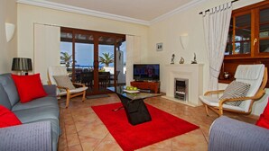 Un salon comprenant un canapé, des fauteuils, un téléviseur, une cheminée et un balcon avec vue.