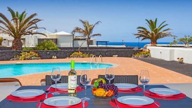 Une table dressée pour un dîner à deux, avec une bouteille de vin, un saladier de fruits et une vue sur une piscine et l’océan.