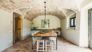 A spacious dining area with a long wooden table and chairs, a brick ceiling, and a window with a view. - Villa Cervia - Six Bedroom Villa, Sleeps 15 (Cervià de Ter)