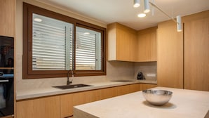 A modern kitchen with wooden cabinets, a large window with blinds, a sink, and a countertop with a bowl. - Villa Lliris - Four Bedroom Villa, Sleeps 10 (Platja d'Aro)