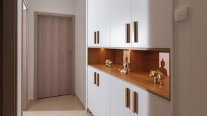 Ein Flur mit einer Holztür, weißen Schränken mit Holzgriffen und einem Regal mit Dekorationsobjekten.