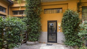 A building with a yellow facade, a black door, and potted plants. - Marcona, 1 - Quiet two-room Milanese apartment (Milan)