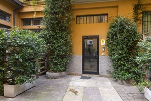 Ein Gebäude mit gelber Fassade, schwarzem Eingang und Blumentöpfen.