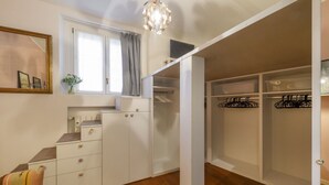 A room with a wooden floor, a white wardrobe, a small desk, a chair, a window with curtains, and a hanging light fixture. - Marcona, 1 - Quiet two-room Milanese apartment (Milan)