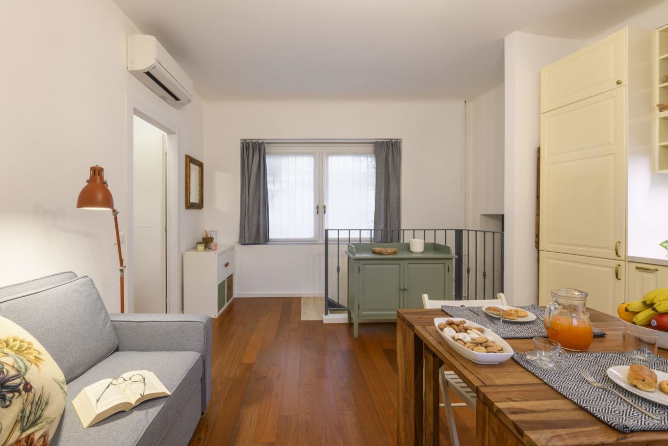Une pièce comprenant un canapé, une table à manger avec des assiettes et un pichet, une fenêtre avec des rideaux et un buffet.