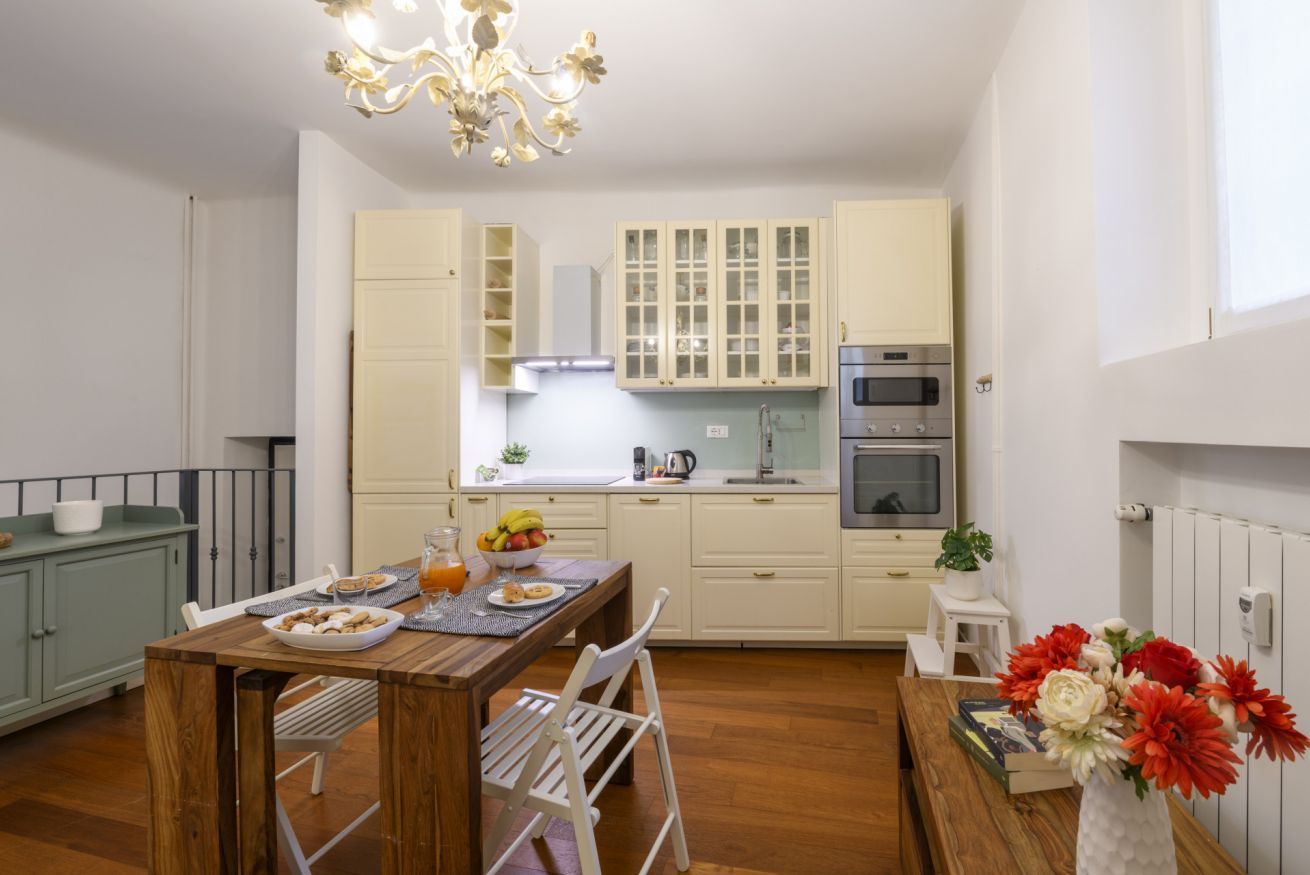 A modern kitchen with white cabinets, a dining table with chairs, a chandelier, and a small potted plant.