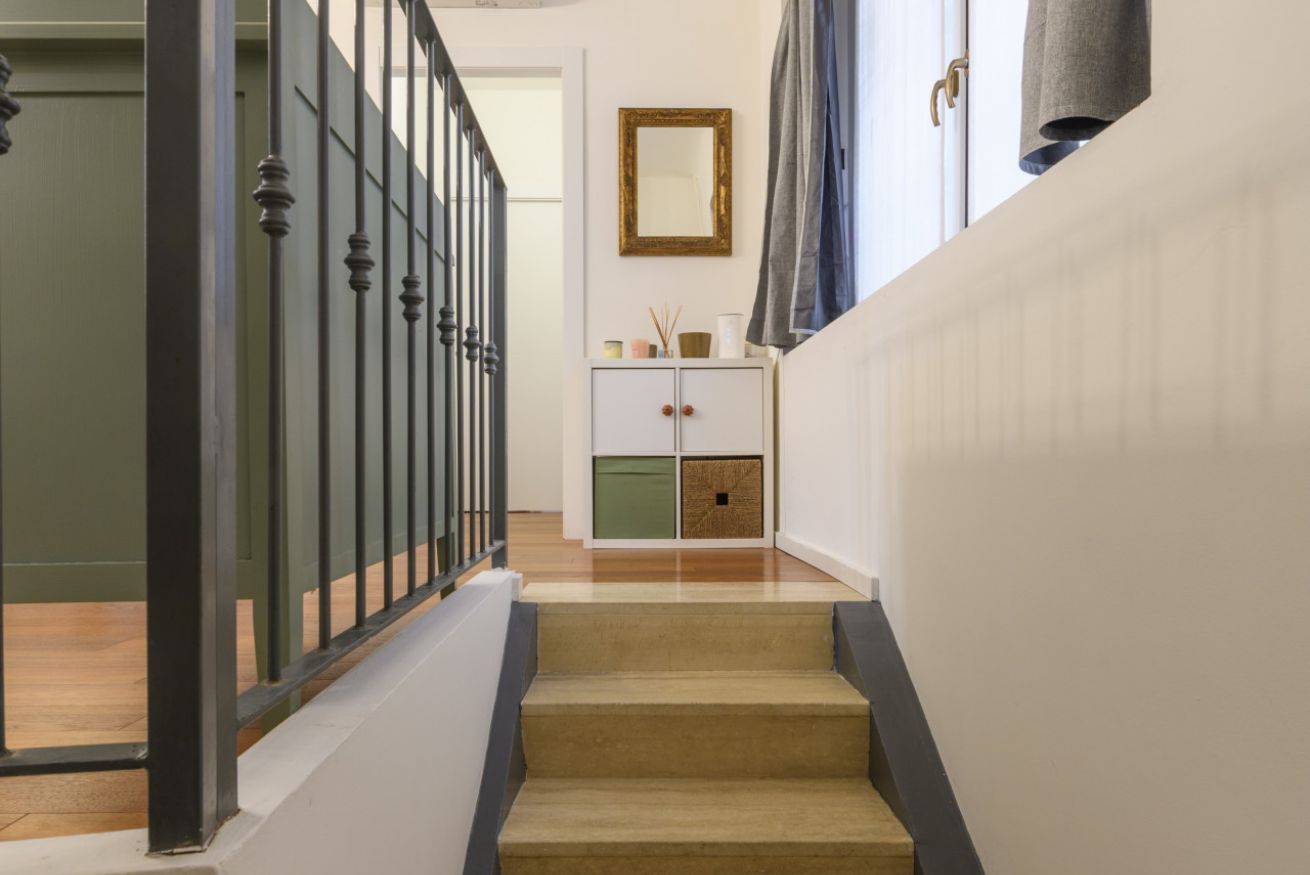 A staircase with a wooden finish, a white wall with a mirror, and a cabinet with drawers and a small shelf.