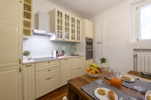 Eine Küche mit weißen Schränken, einem Holztisch und einer Obstschale.