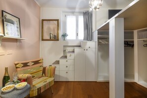 Ein gemütlicher Wohnbereich mit Sofa, einem kleinen Esstisch mit Snacks, einer Weinflasche, einem Spiegel und einem Einbauschrank.