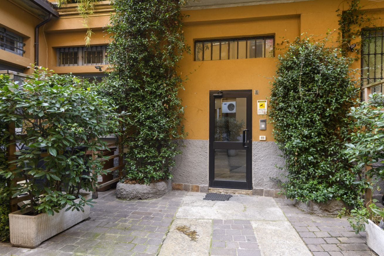 A building with a yellow facade, a black door, and potted plants.