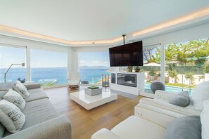 A modern living room with a large TV, comfortable seating, a coffee table, and a view of the ocean. - Luxury Villa Sea Views 6 rooms 12 pax wifi air conditioning (LLucmajor)
