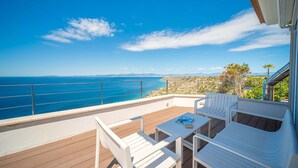 A balcony with white chairs and a table, overlooking a coastal view with the sea and distant land. - Luxury Villa Sea Views 6 rooms 12 pax wifi air conditioning (LLucmajor)