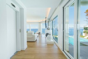 A modern interior with a wooden floor, white furniture, a large window, and a view of the sea. - Luxury Villa Sea Views 6 rooms 12 pax wifi air conditioning (LLucmajor)